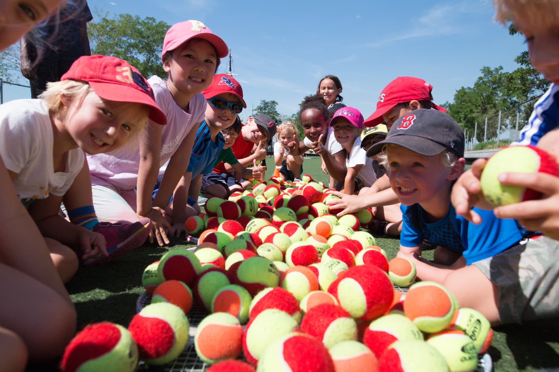 Children smiling around a colorful pile of tennis balls
