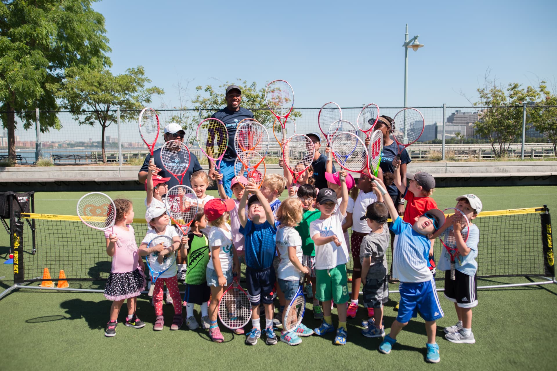 Young Super Duper Tennis players raising their racquets with their coaches
